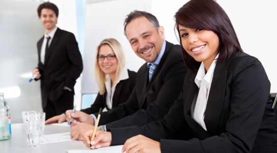 Business people in suits smiling while sitting at a table.